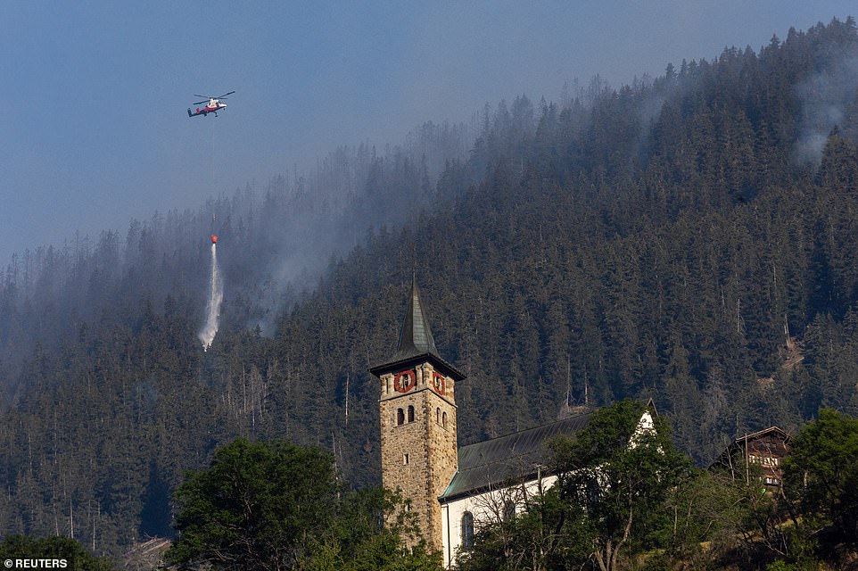 A helicopter carries water to a wildfire on the flank of a mountain in Bitsch near Brig, Switzerland, on Tuesday