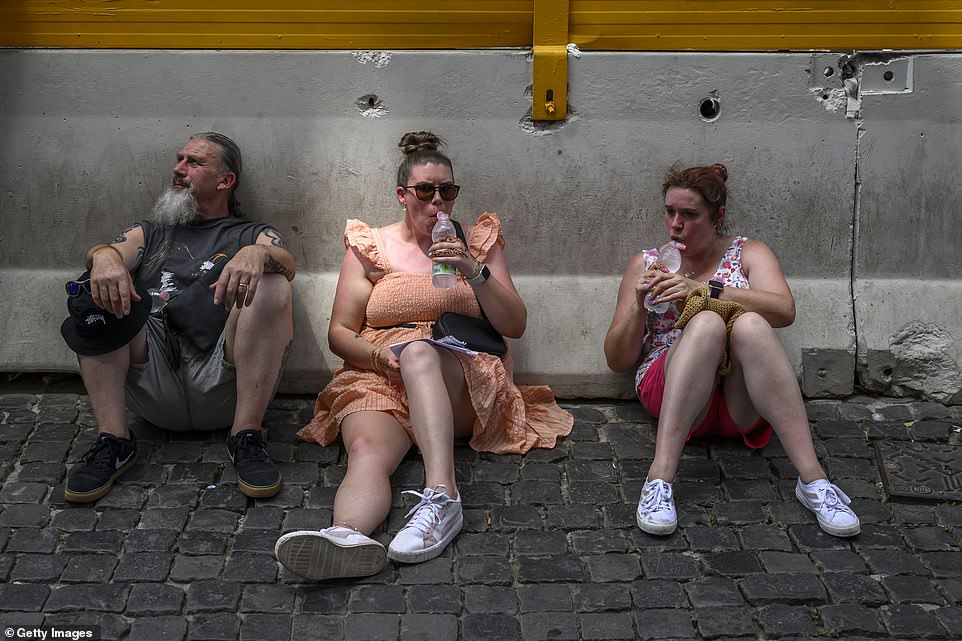 Tourists sit down in the shade and drink water as they try to cool down during a heat wave in Rome, Italy, on Monday