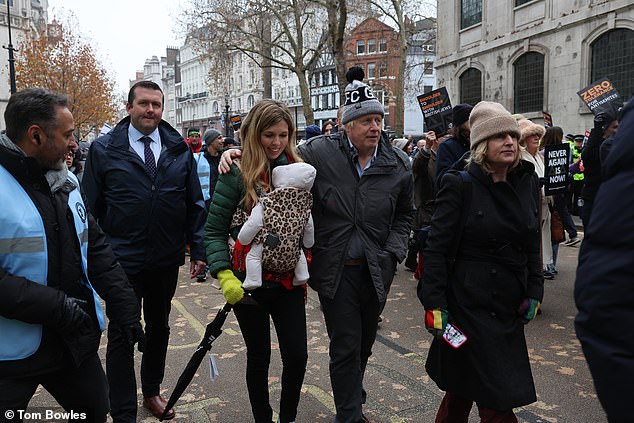 Mr Johnson, 59, appeared bundled up against the biting temperatures in a woolly hat, while 35-year-old Carrie held their child together in a baby carrier