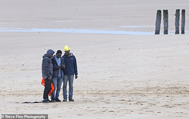 A group of migrants seen walking back along a beach in Calais today following a failed attempt at a crossing