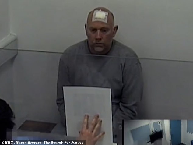 Couzens looks at a picture of Sarah Everard as it is held up to a protective screen while he is being quizzed by detectives at Wandsworth police station in London